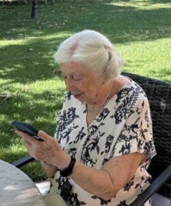 Mujer de 95 años utilizando un teléfono móvil en un parque, reflejando aprendizaje, autonomía y participación en la vida cotidiana.