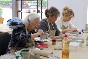 Magdalena, de 95 años, trabajando con arcilla en su taller de cerámica junto a dos compañeras.